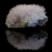 Mesolite acicular crystal spray over pale green apophyllite cluster reflected on black surface, macro photography by Minerals Photography