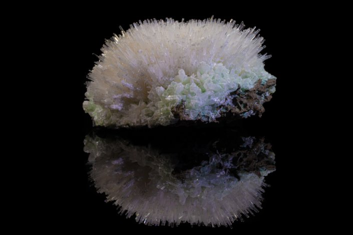 Mesolite acicular crystal spray over pale green apophyllite cluster reflected on black surface, macro photography by Minerals Photography
