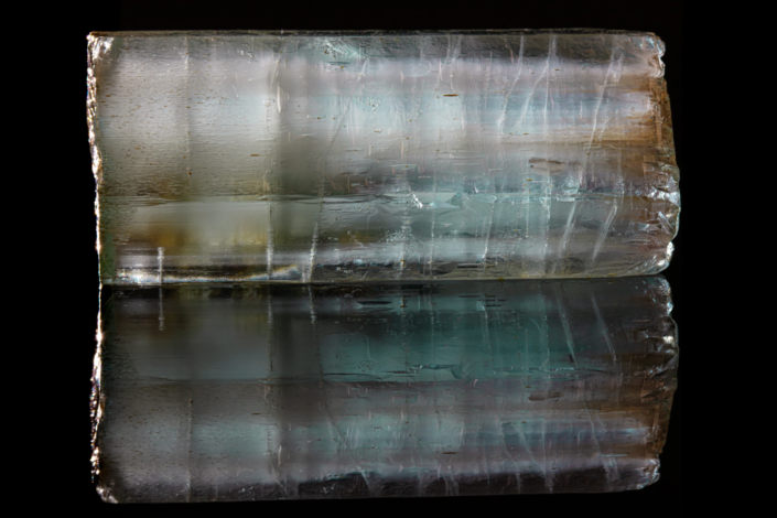 Aquamarine crystal — horizontal macro view on black mirror background showing internal teal color zoning and mirror reflection