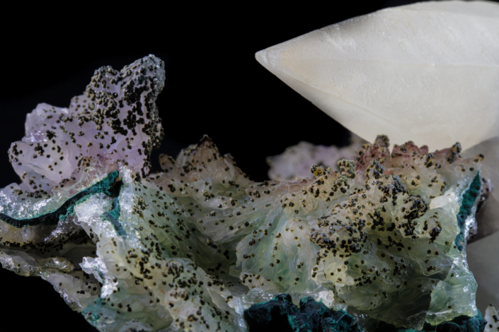 Calcite phantom on malachite — macro view showing green and pink spotted matrix with calcite blade tip and teal malachite border