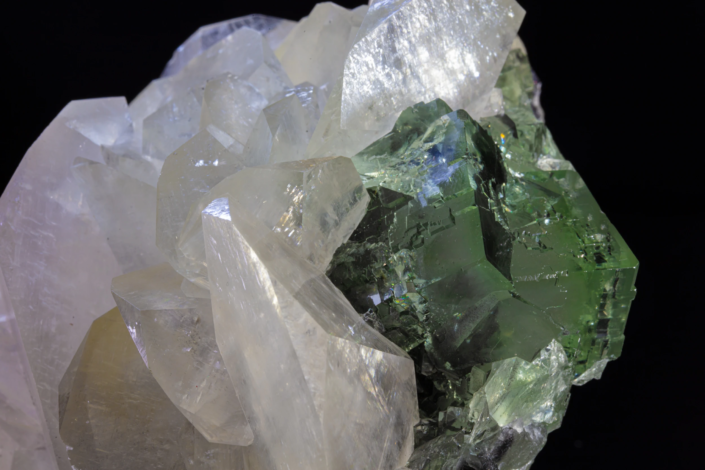 Calcite on fluorite — macro close-up showing transparent green fluorite cube with blue internal reflections surrounded by white calcite crystals