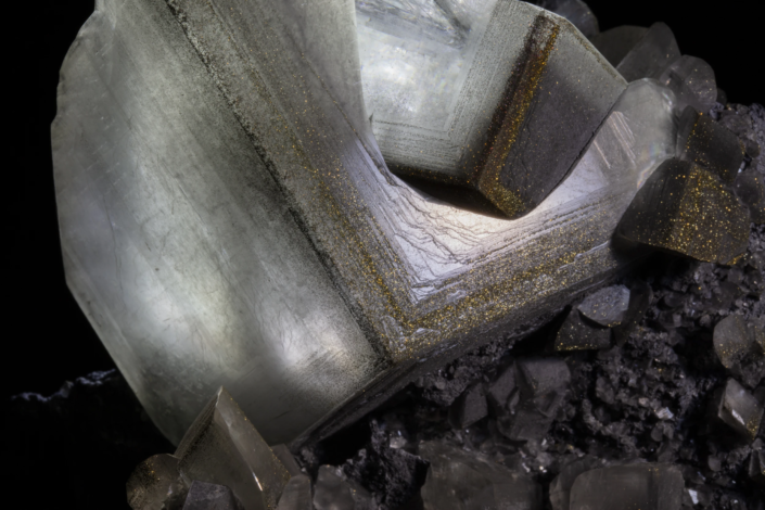 Calcite with pyrite — macro close-up showing concentric growth bands with gold pyrite micro-crystal dust along crystal edges and concavity