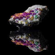 Chalcopyrite with dolomite mineral specimen — full view on black mirror background showing iridescent magenta gold and teal chalcopyrite crystals on white dolomite matrix, macro photography by Minerals Photography