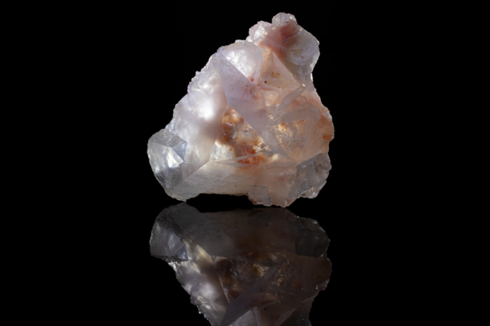 Full specimen view of white twinned dolomite crystal cluster with peach iron oxide inclusions on black reflective surface — macro photography by Minerals Photography