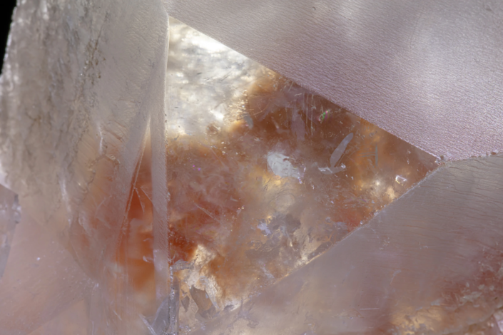 Deep macro view through twinned dolomite crystal faces revealing translucent amber and iron-stained interior zones with iridescent light diffraction — macro photography by Minerals Photography