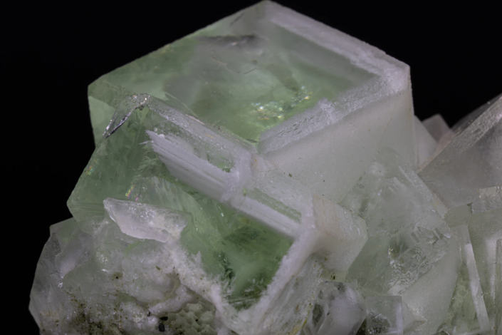 Extreme close-up of a large pale green fluorite cubic crystal face revealing stepped cleavage, internal translucency, and rainbow light diffraction — macro photography by Minerals Photography
