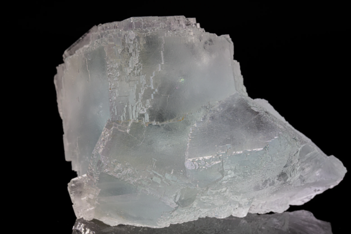 Close-up of pale blue-green etched fluorite crystal showing stepped dissolution terraces across large cubic faces with iridescent light spots — macro photography by Minerals Photography