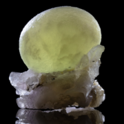 Single large yellow-green botryoidal fluorite sphere resting on white quartz crystal cluster with black mineral inclusions and mirror reflection on black background — macro photography by Minerals Photography