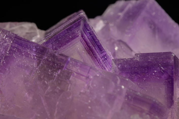 Close macro of pale lavender fluorite cubic crystals with sharp purple-edged growth rims and stepped faces rising above a mass of smaller crystals — macro photography by Minerals Photography