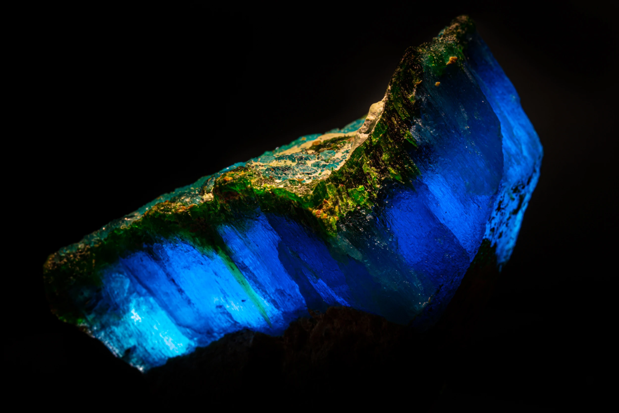 Krohnkite and natrochalcite specimen illuminated from behind, revealing deep electric blue translucency and green mineral veining, macro photography by Minerals Photography