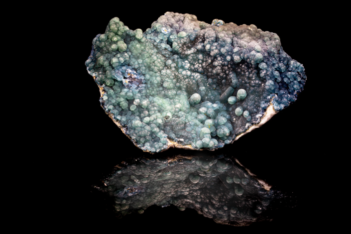 Plumbogummite specimen with green and blue-gray botryoidal aggregates on dark matrix reflected on black surface, macro photography by Minerals Photography