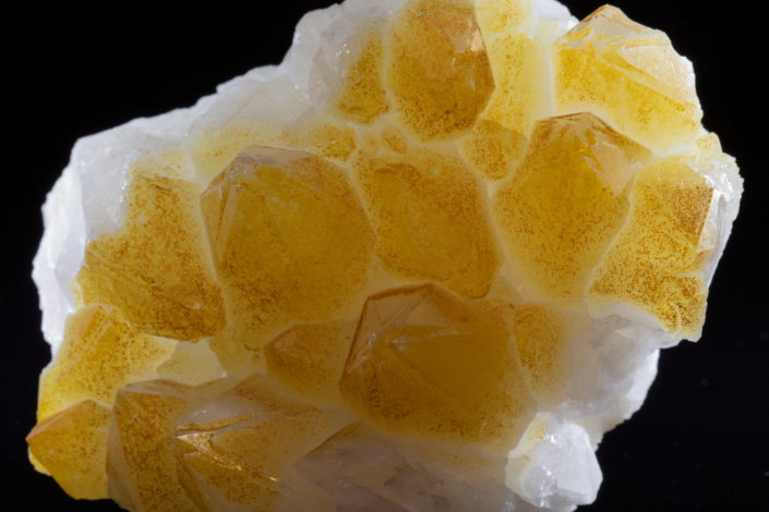 Close-up of quartz crystals with yellow-orange iron oxide surface coating showing rhombohedral terminations on white matrix, macro photography by Minerals Photography