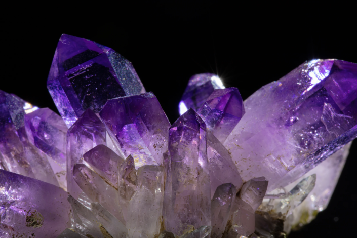 Macro of amethyst quartz crystals showing vivid purple color zoning and internal reflections with smaller secondary crystals at the base, macro photography by Minerals Photography
