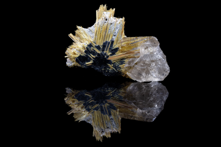 Golden rutile needles radiating from black hematite rosette with quartz crystal reflected on black mirror surface, macro photography by Minerals Photography