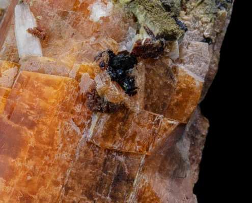 Macro of serandite orange crystal faces with stepped cleavage and dark black lustrous accessory mineral cluster, macro photography by Minerals Photography