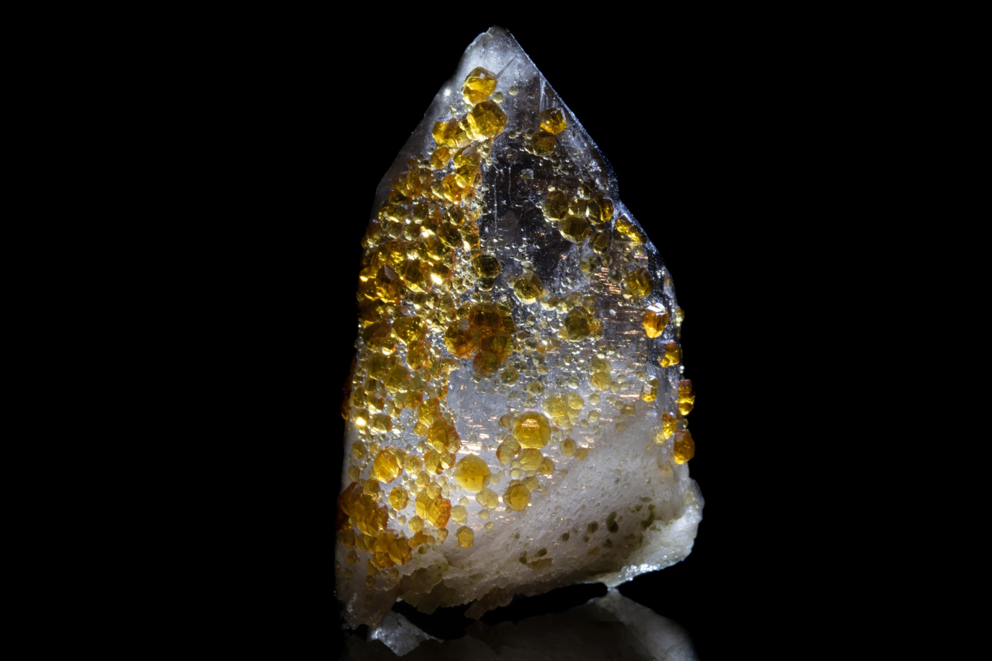 Spessartine garnet golden-orange crystals of varying sizes scattered over transparent quartz point on black background, macro photography by Minerals Photography